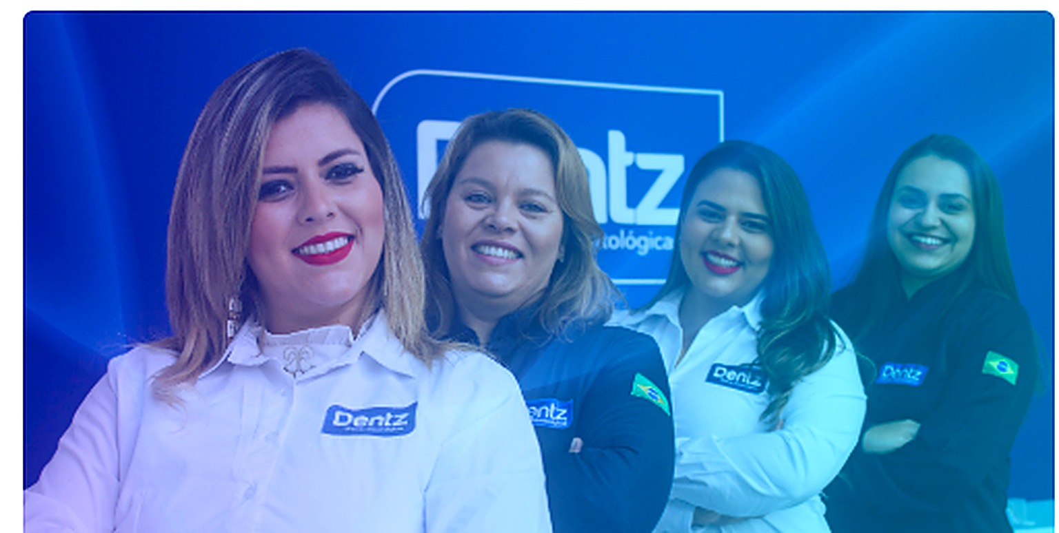 Equipe da Dentz Rio Preto sorrindo em frente à parede azul da clínica